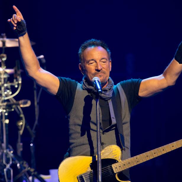 Bruce Springsteen tritt mit erhobenen Armen und Gitarre auf einer Bühne auf.