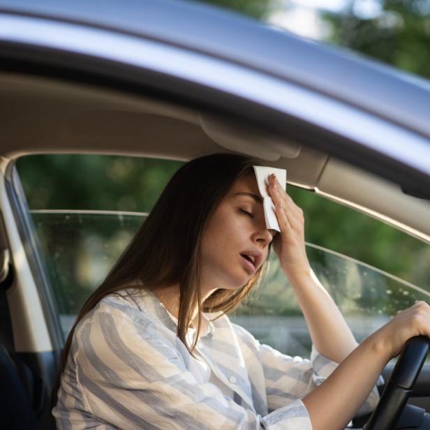 Eine erschöpfte Frau wischt sich den Schweiß von der Stirn im Auto.