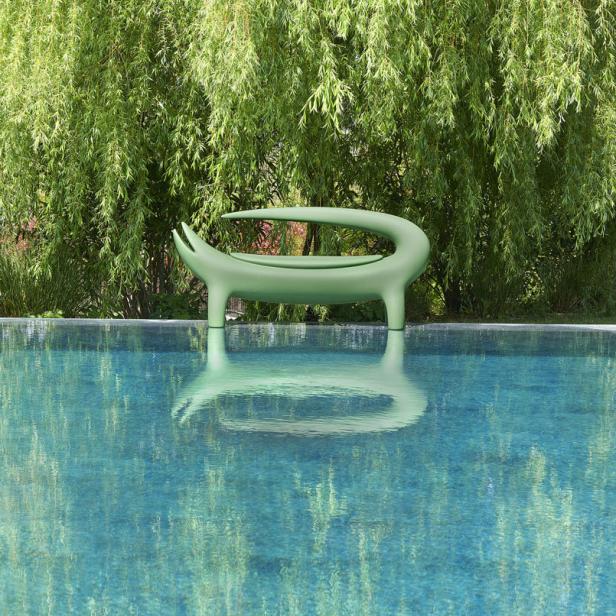 Eine grüne, moderne Liege steht am Rande eines Pools unter einem Baum.