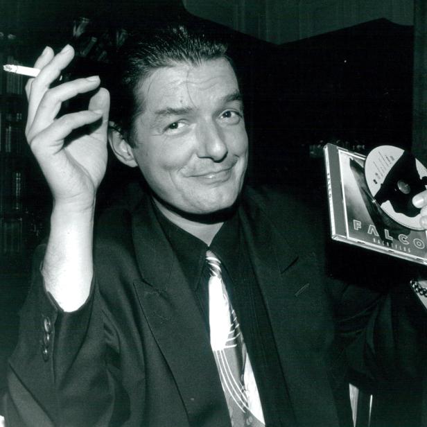 Falco hält eine Zigarette und sein Album „Nachtflug“ in der Hand.