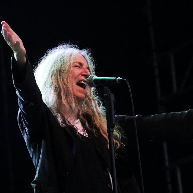 Patti Smith singt mit erhobenen Armen auf der Bühne.