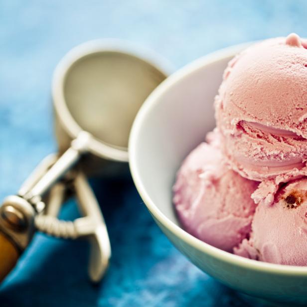 Eine Schale mit rosa Eiscreme und einem Eisportionierer auf blauem Hintergrund.