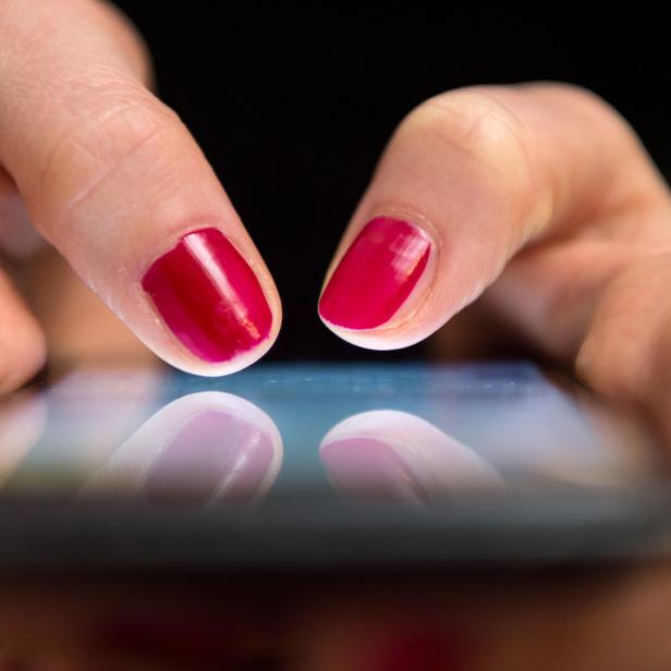 Eine Frau tippt mit rot lackierten Fingernägeln auf ein Smartphone.