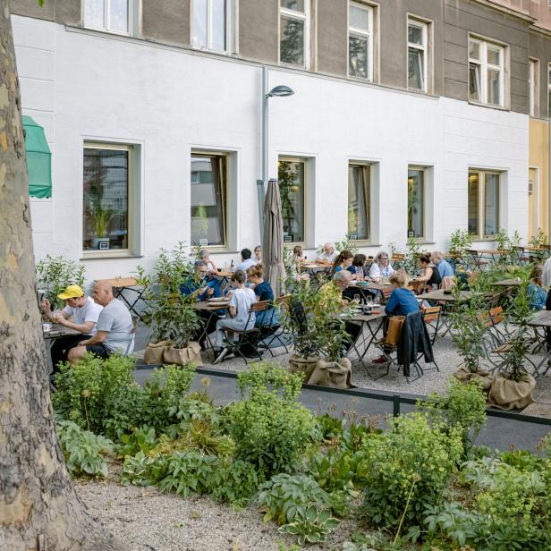 Ein Außenbereich eines Restaurants mit mehreren Tischen und Gästen, umgeben von Grünpflanzen.