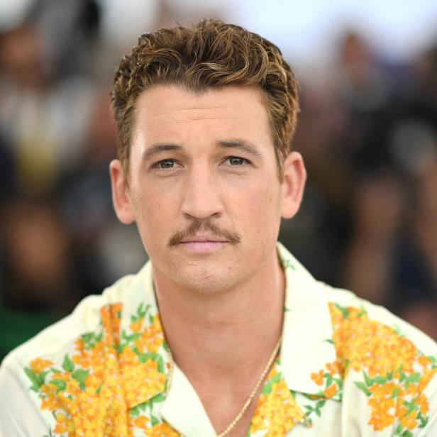 Ein Porträt von Miles Teller mit Schnurrbart und einem Hemd mit gelben Blumen.