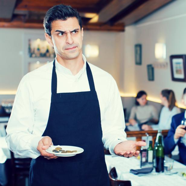 Ein unzufriedener Kellner hält ein kleines Trinkgeld in einem Restaurant.