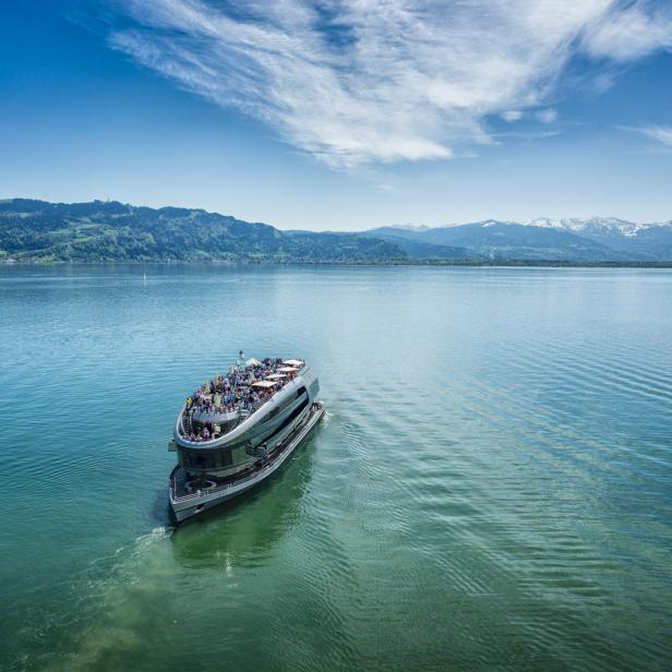 Ein Ausflugsschiff fährt auf einem See vor einer Bergkulisse.
