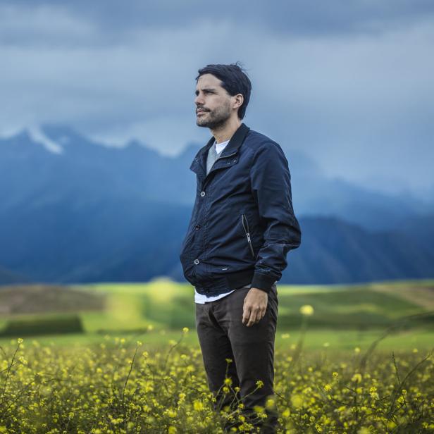 Ein Mann steht auf einem Feld mit gelben Blumen und blickt in die Ferne.