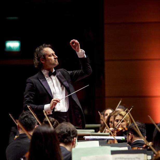 Ein Dirigent leitet ein Orchester mit Geigen.