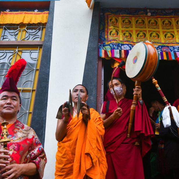 Buddhistische Mönche spielen Musikinstrumente vor einem verzierten Gebäude.