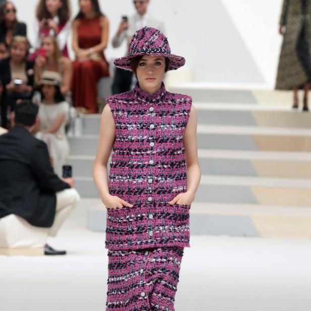 Eine Frau in einem pinkfarbenen Tweed-Ensemble mit Hut und Stiefeln auf einem Laufsteg.