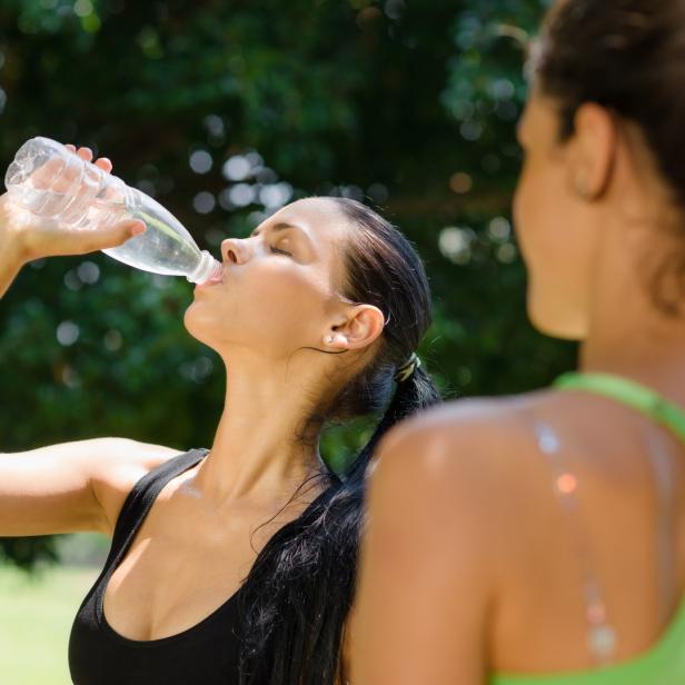 Eine Frau trinkt Wasser aus einer Plastikflasche, während eine andere Frau im Hintergrund steht.