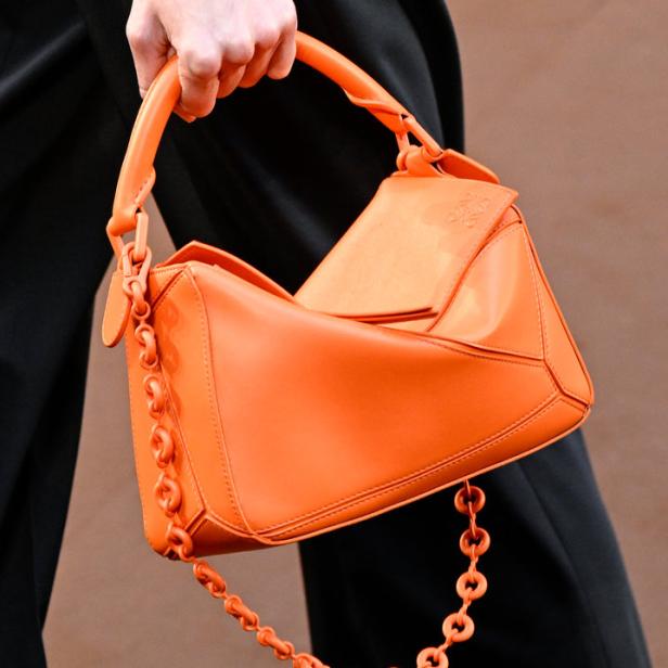 Eine Person hält eine orangefarbene Loewe Puzzle Bag mit Kettenelementen.