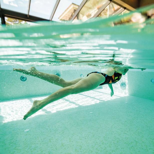 Eine Frau schwimmt in einem Schwimmbad unter einer Glasdecke.