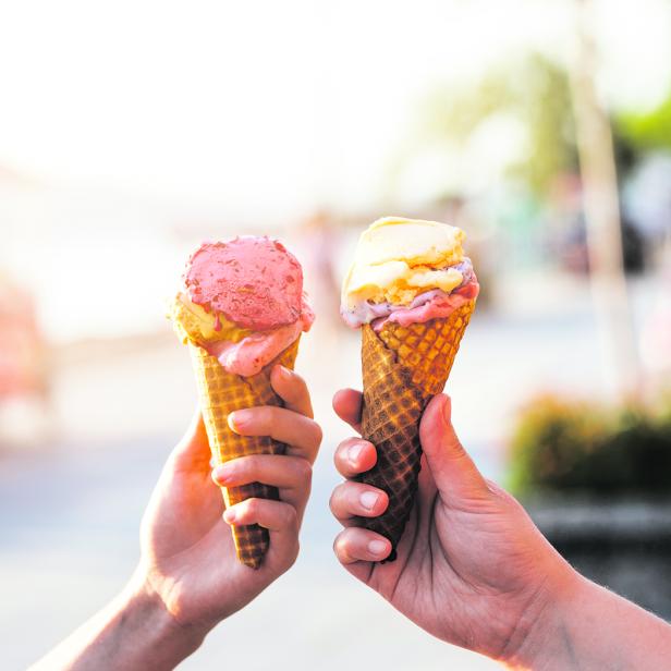 Zwei Hände halten Eiswaffeln mit rosa und gelbem Eis.