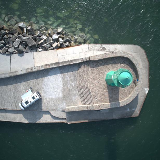 Ein Wohnmobil steht neben einem grünen Leuchtturm auf einer Mole im Wasser.