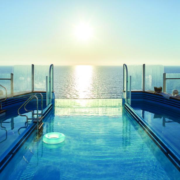 Ein Schwimmbecken auf einem Kreuzfahrtschiff mit Blick auf das Meer bei Sonnenaufgang.