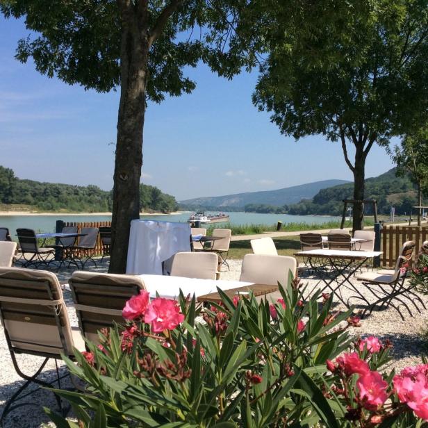 Ein Restaurantgarten mit Blick auf einen Fluss an einem sonnigen Tag.