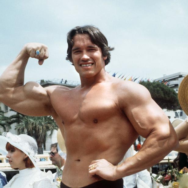 Arnold Schwarzenegger posiert am Strand und zeigt seine Muskeln.