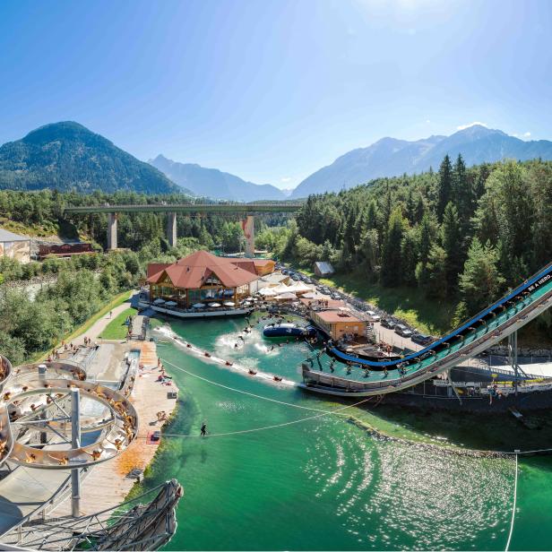 Panoramablick auf ein Freizeitbad in den Bergen mit Rutschen und Badeseen.