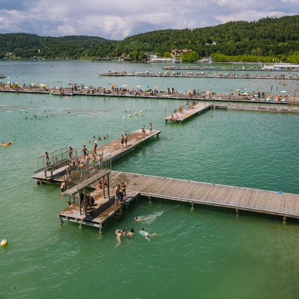 Ein belebtes Strandbad mit Badegästen auf Stegen und im türkisfarbenen Wasser.