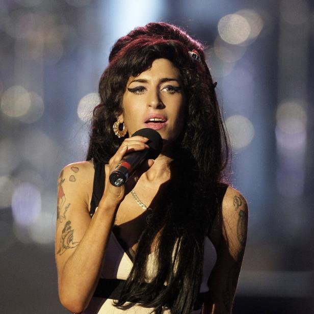 Amy Winehouse singt mit einem Mikrofon in der Hand auf einer Bühne.