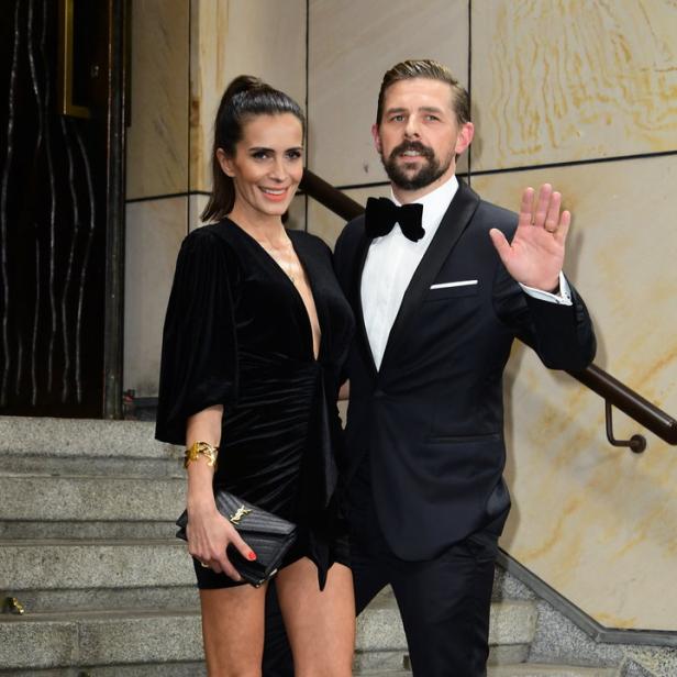 Ein Mann im Smoking und eine Frau im schwarzen Kleid posieren auf einer Treppe.