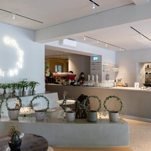 Innenansicht eines Cafés mit Pflanzen und einer leuchtenden Neonreklame.