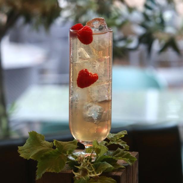 Ein Cocktail mit Eis und Himbeeren steht auf einer Holzkiste.