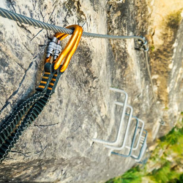 Ein Klettersteig mit Stahlseil, Karabiner und Trittstufen an einer Felswand.