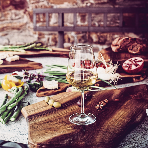 Ein Tisch mit einem Glas Weißwein, Käse, Brot, Spargel und anderen Speisen angerichtet.