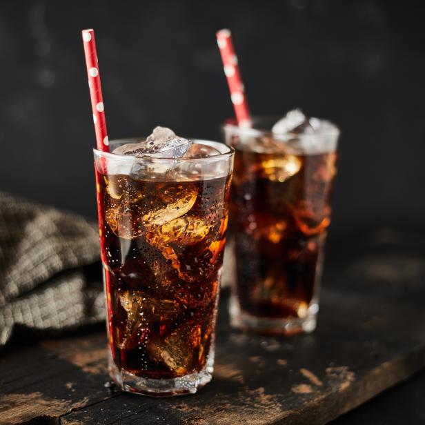 Zwei Gläser Cola mit Eis und roten Strohhalmen auf einem Holztisch.