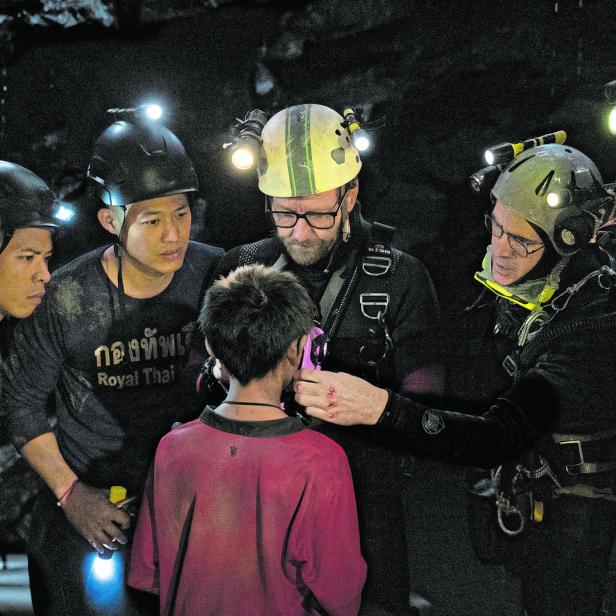 Ein Taucher befestigt Ausrüstung an einem Jungen in einer dunklen Höhle, umgeben von Helfern.