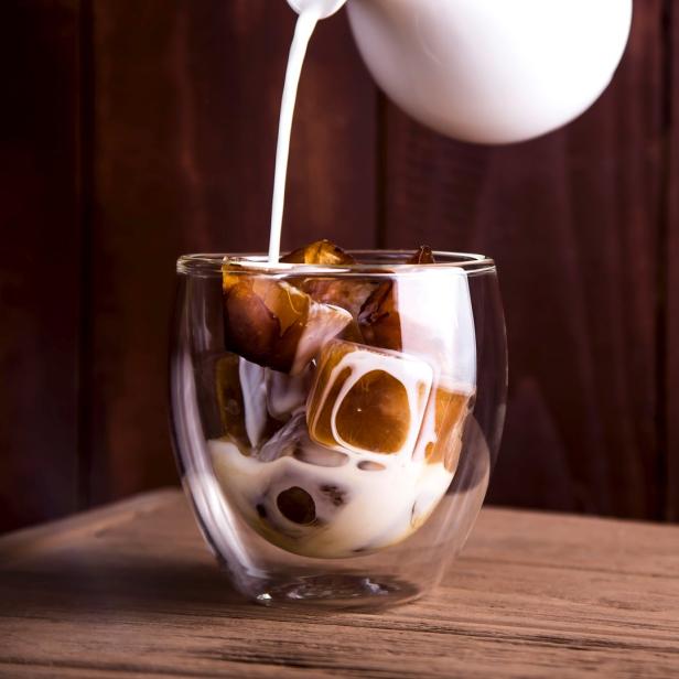 Milch wird in ein Glas mit Kaffee-Eiswürfeln gegossen.