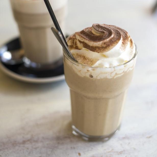Ein Glas Eiskaffee mit Schlagsahne und Kakaopulver steht auf einem Tisch.