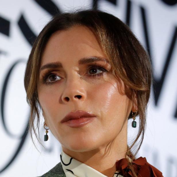 Nahaufnahme von Victoria Beckham mit grünen Ohrringen und einer verzierten Bluse.