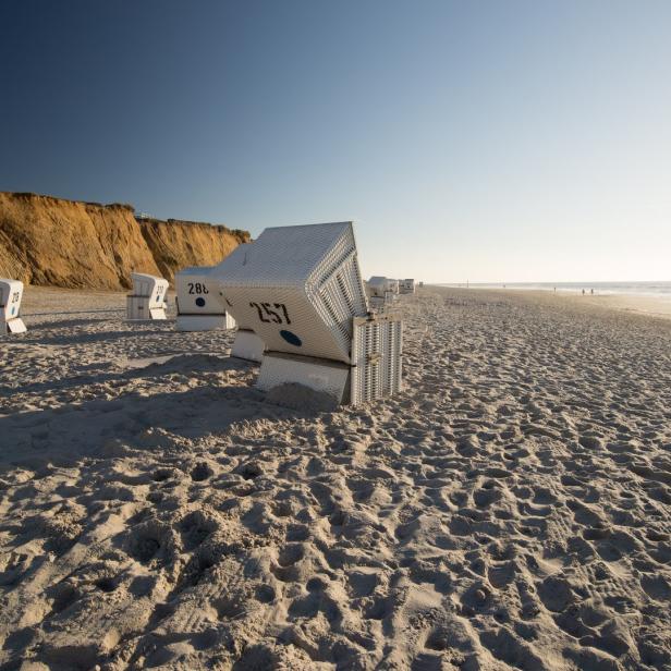 Strandkörbe stehen am Strand unterhalb einer Küstenklippe.