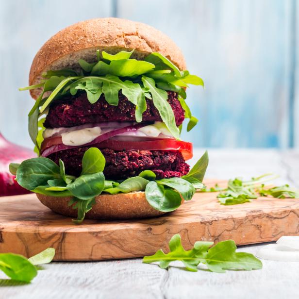 Ein doppelter Rote-Bete-Burger mit Salat, Tomaten und Zwiebeln auf einem Holzbrett.