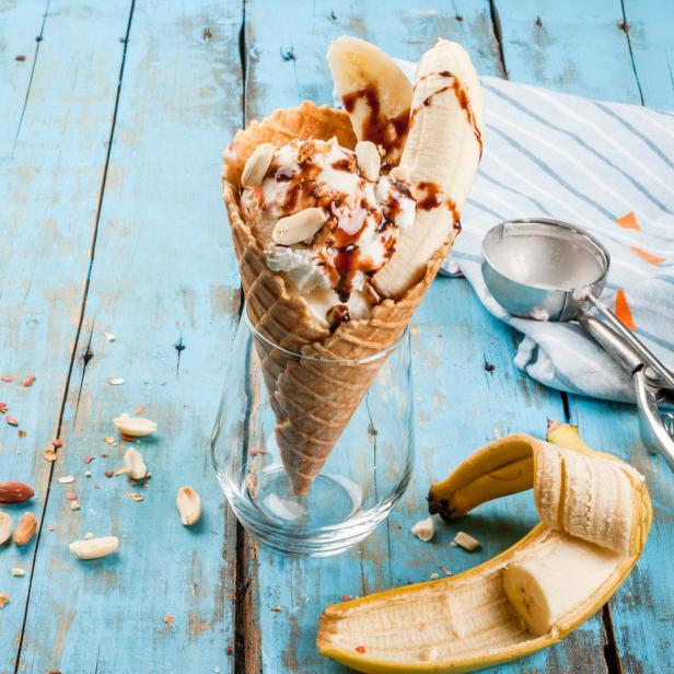 Ein Eisbecher mit Banane, Schokoladensoße und Erdnüssen auf einem blauen Holztisch.