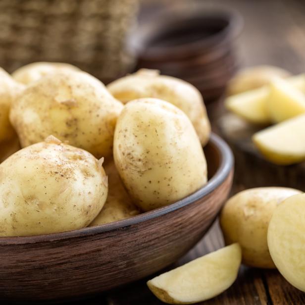 Einige Kartoffeln in einer braunen Schüssel auf einem Holztisch.