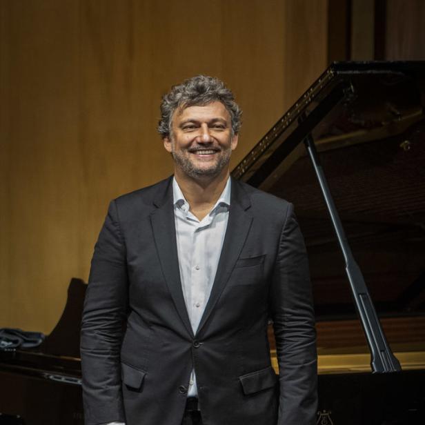 Ein Mann in einem Anzug steht lächelnd vor einem Steinway-Flügel.
