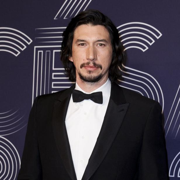 Adam Driver in einem schwarzen Smoking vor einem grafischen Hintergrund.