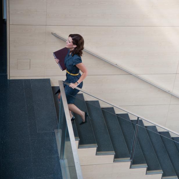 Eine Frau in einem blauen Kleid steigt eine Treppe mit einem Ordner in der Hand hinauf.