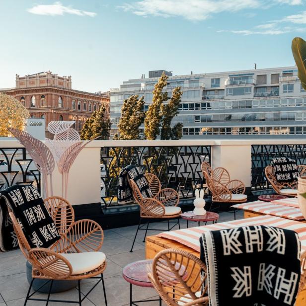 Eine Dachterrasse mit Korbstühlen, Tischen und Blick auf Gebäude in der Stadt.