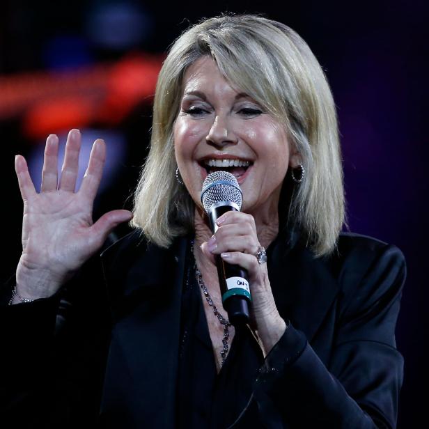 Olivia Newton-John singt bei einer Veranstaltung und winkt ins Publikum.