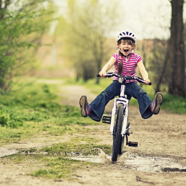 Ein Mädchen mit Helm fährt freihändig auf einem Feldweg Fahrrad.