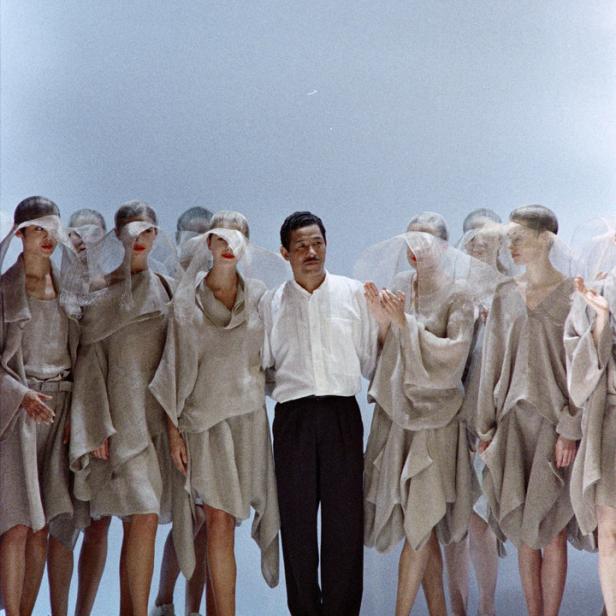 Ein Modedesigner steht mit Models in beigen Kleidern und Schleiern auf dem Laufsteg.