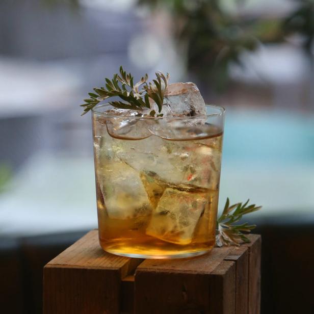 Ein Cocktail mit Eiswürfeln und einer Garnitur aus Grünzeug steht auf einer Holzkiste.