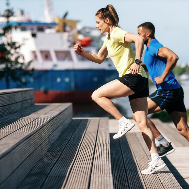 Eine Frau und ein Mann joggen eine Holztreppe hinauf.