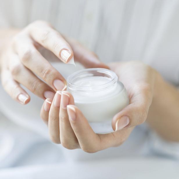 Eine Frau hält ein Glas mit weißer Creme in ihren Händen.